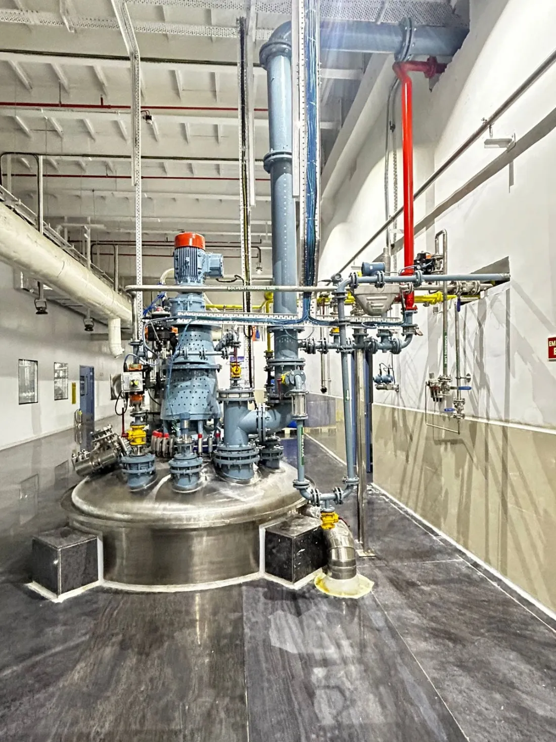 Reactor fitted with a gearbox, lined piping and instrument valves inside an API plant hall